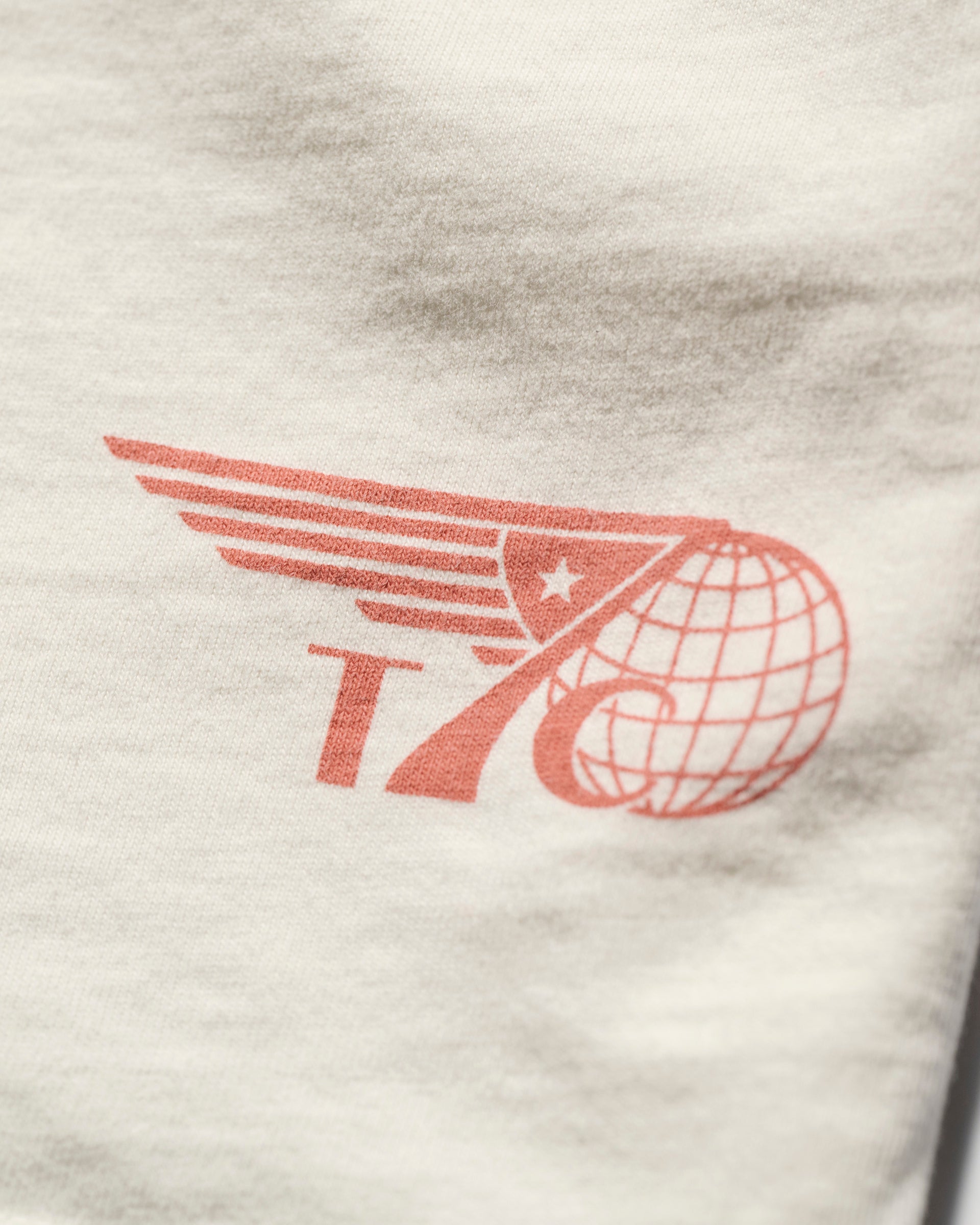 The T7C THE KNOXS TEE WITH ICON PRINT features a red graphic with the number 76, a wing, globe, and star on white fabric, with the design printed in the corner.