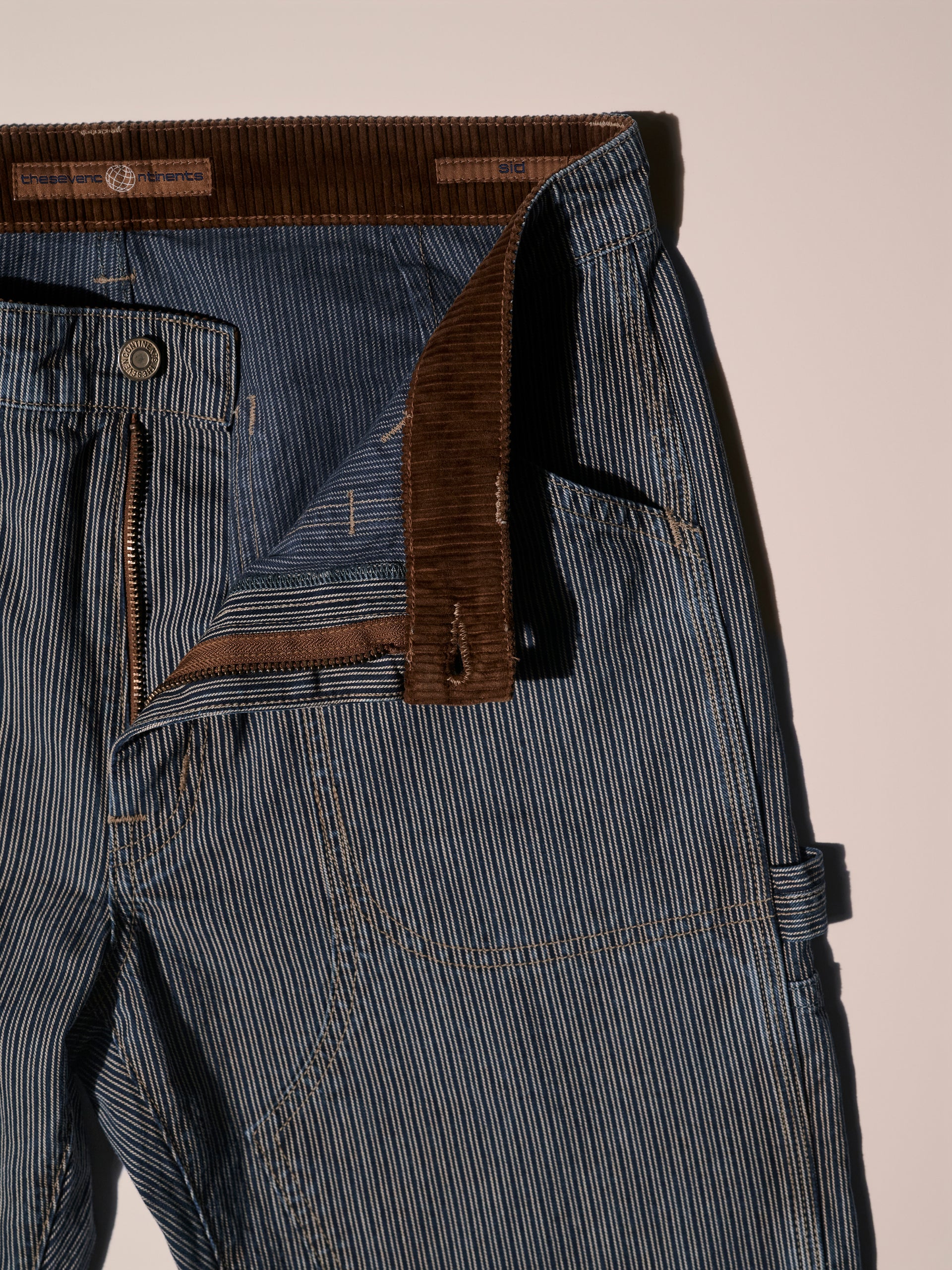 A detail image of a blue and white railroad stripe carpenter pant with a corduroy detail in the inner waist band