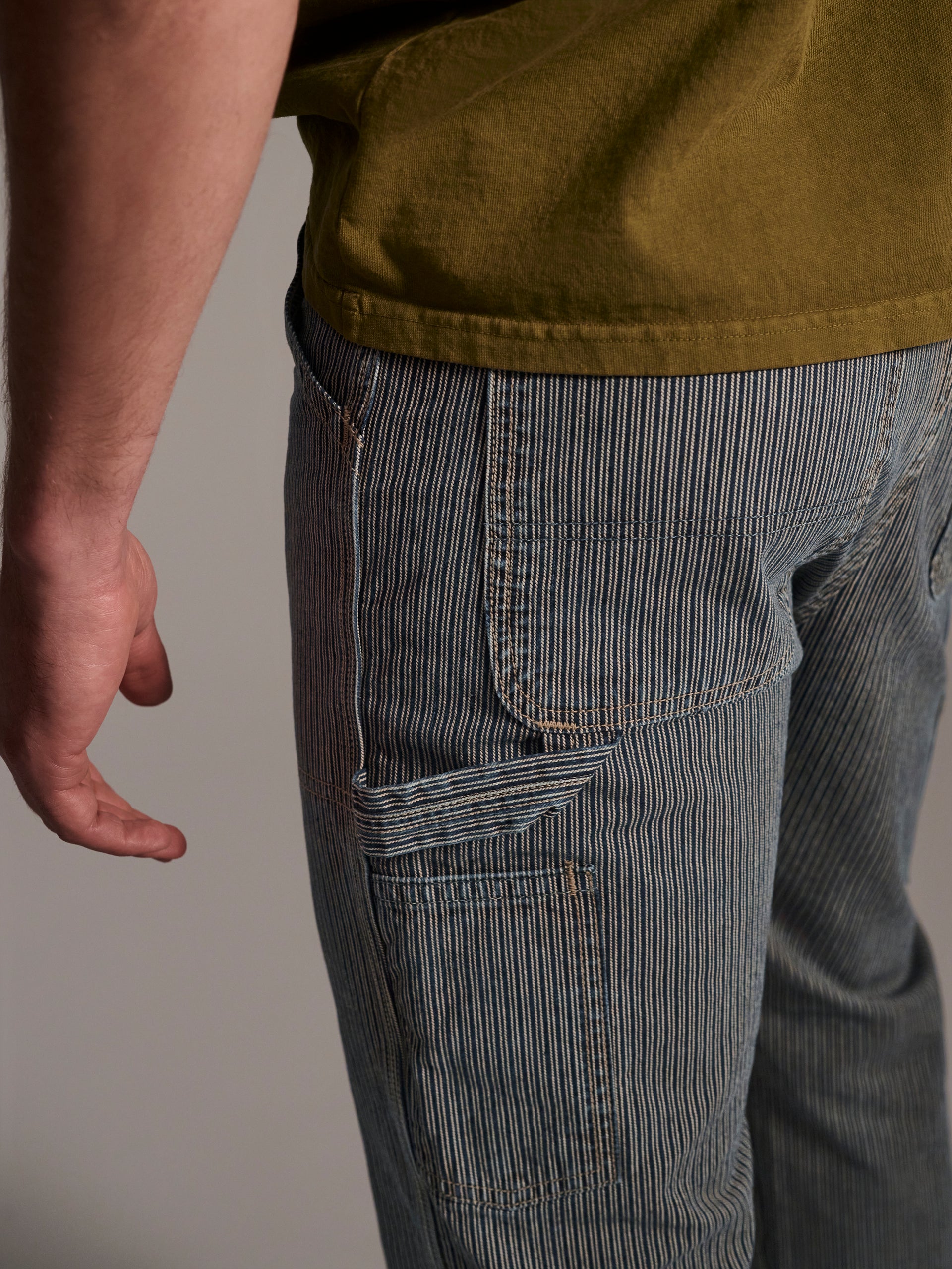 A detail image of a male model wearing a blue and white railroad stripe carpenter pant