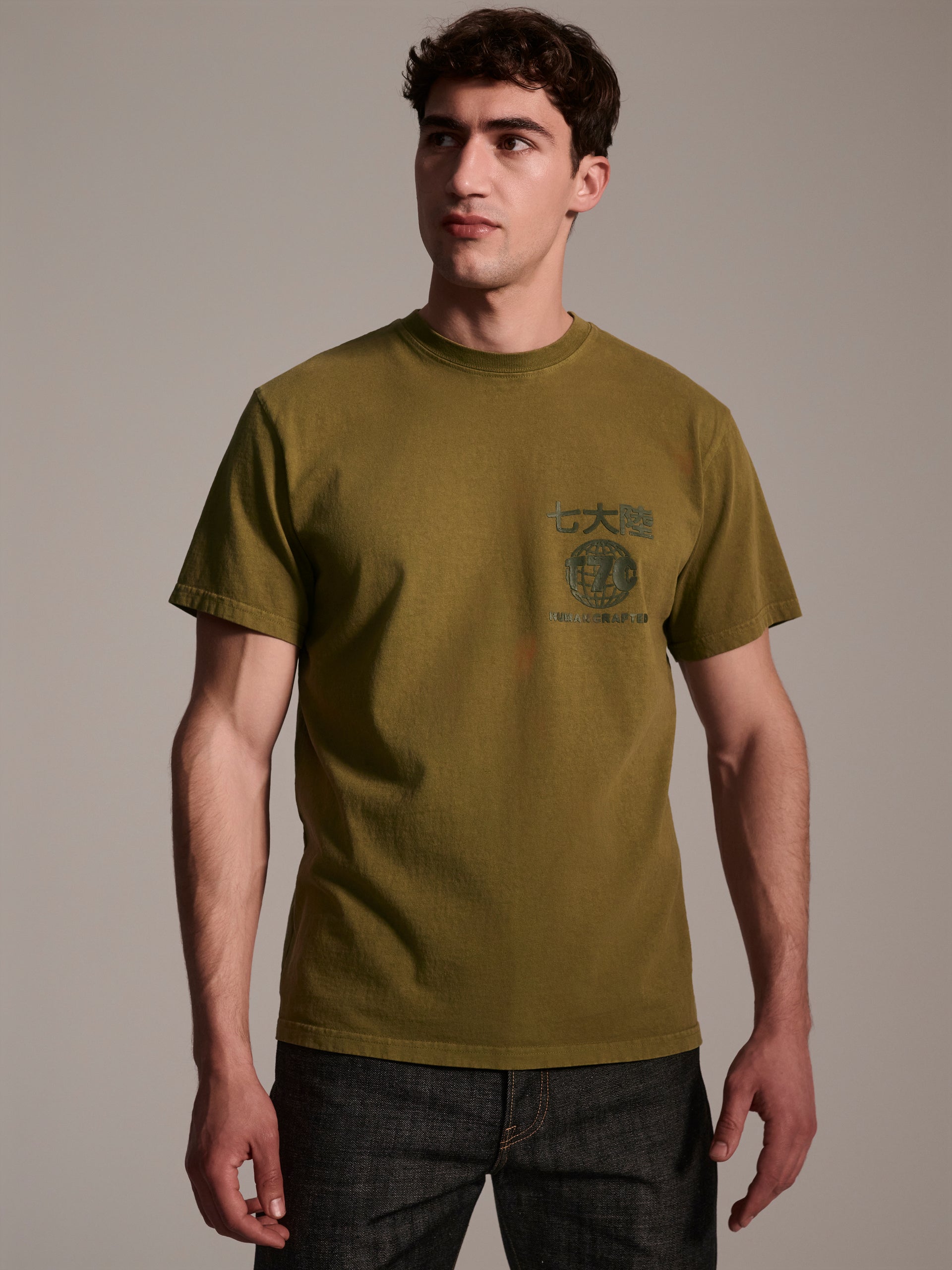 A male model wearing a olive t-shirt with a logo detail