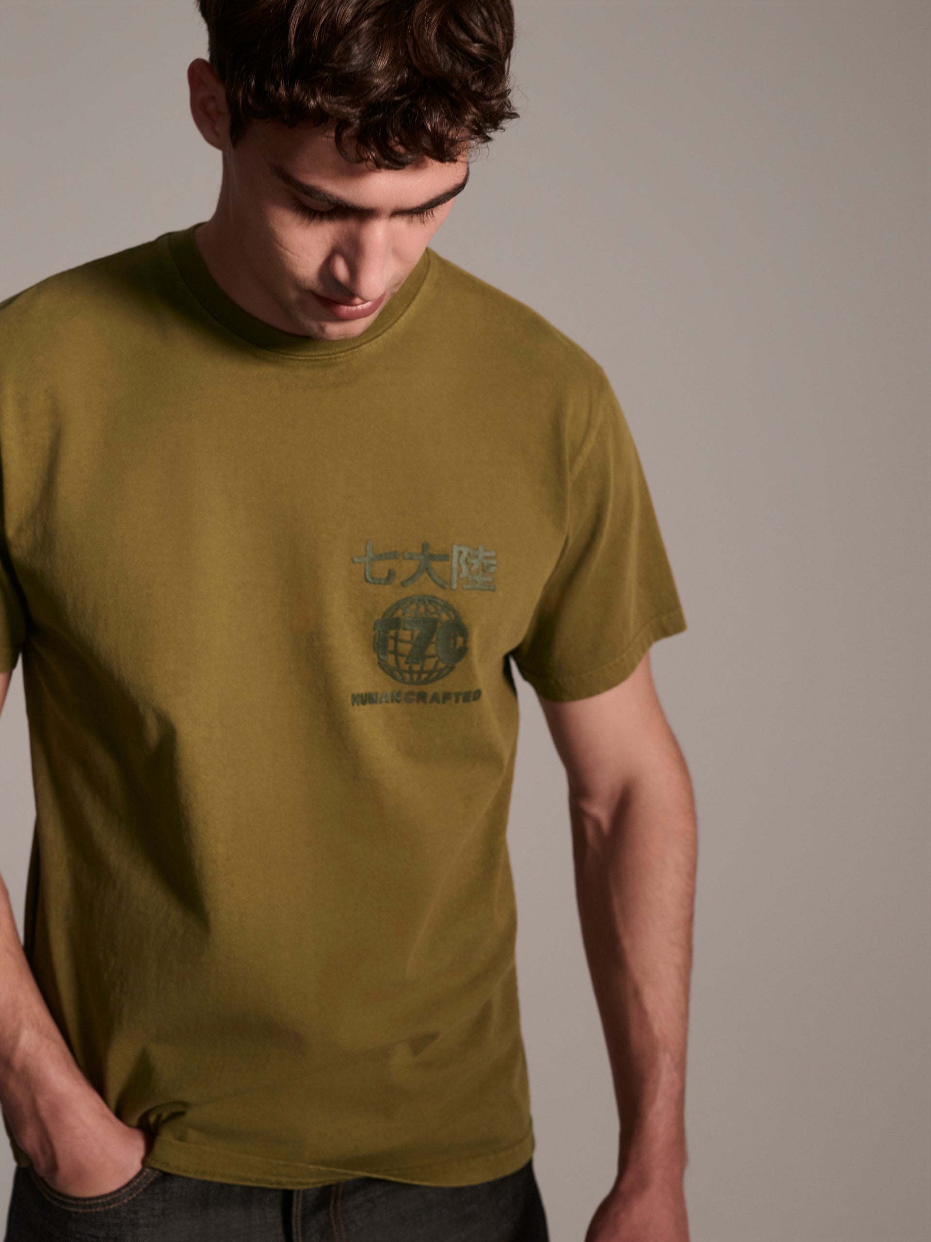 A male model wearing a olive t-shirt with a logo detail