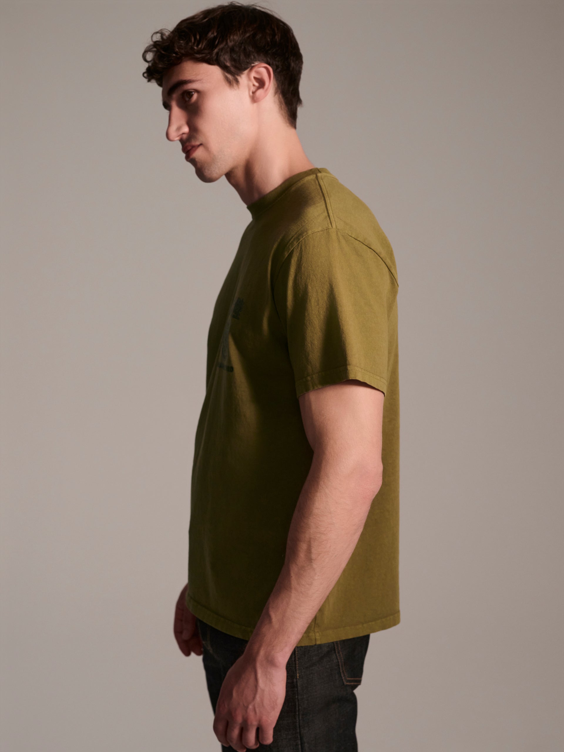 A profile image of a male model wearing a olive t-shirt with a logo detail