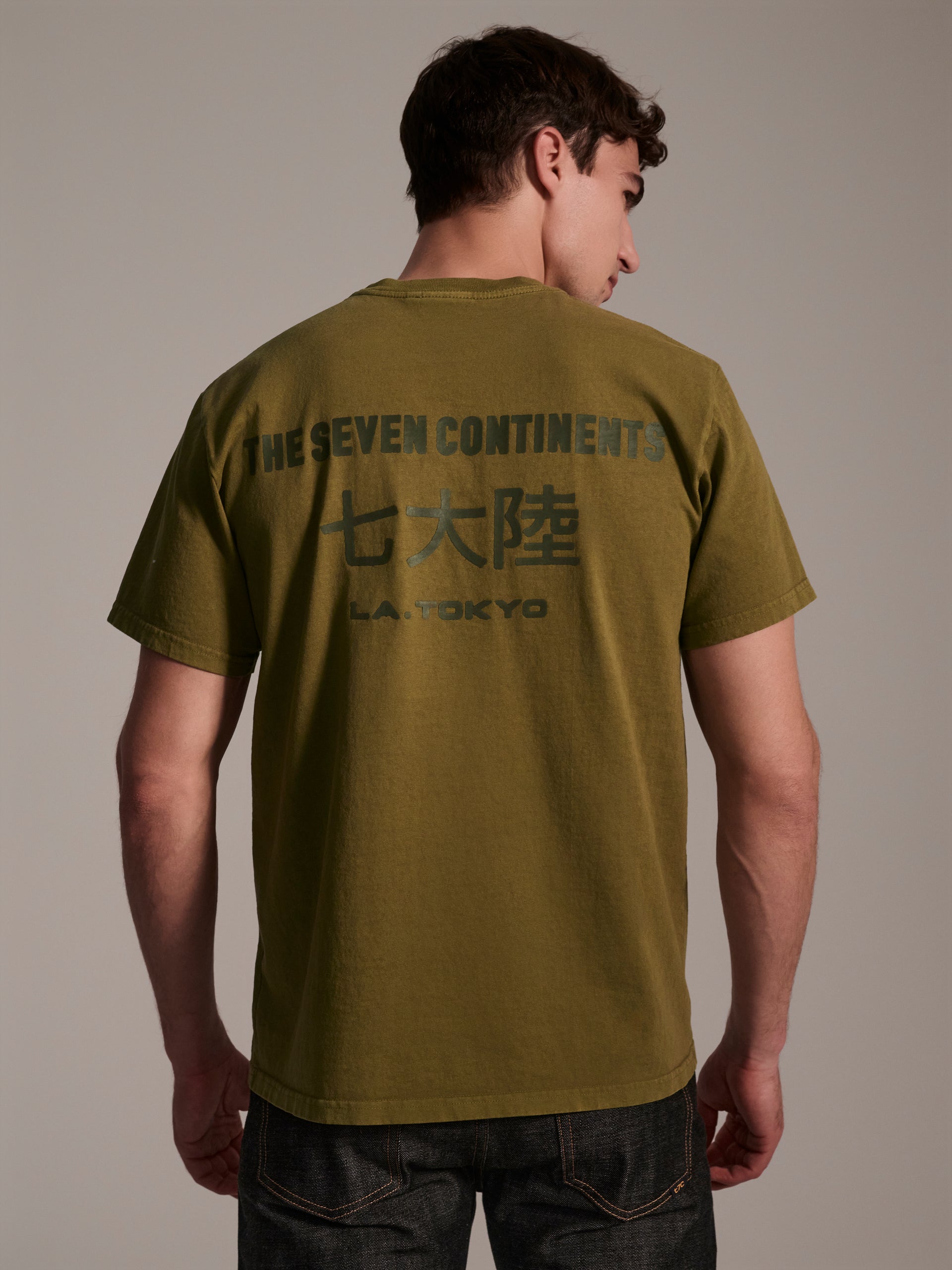 A back image of male model wearing a olive t-shirt with a logo detail