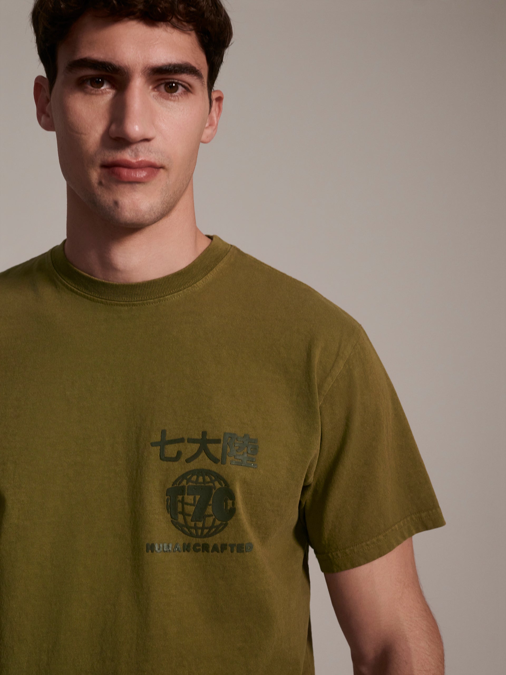 A detail image of a male model wearing a olive t-shirt with a logo detail