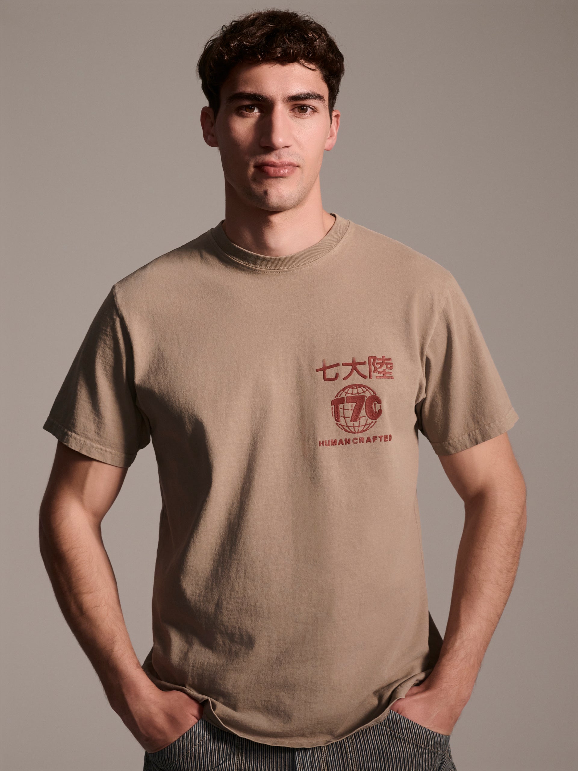 A male model in a beige t-shirt with a red logo detail