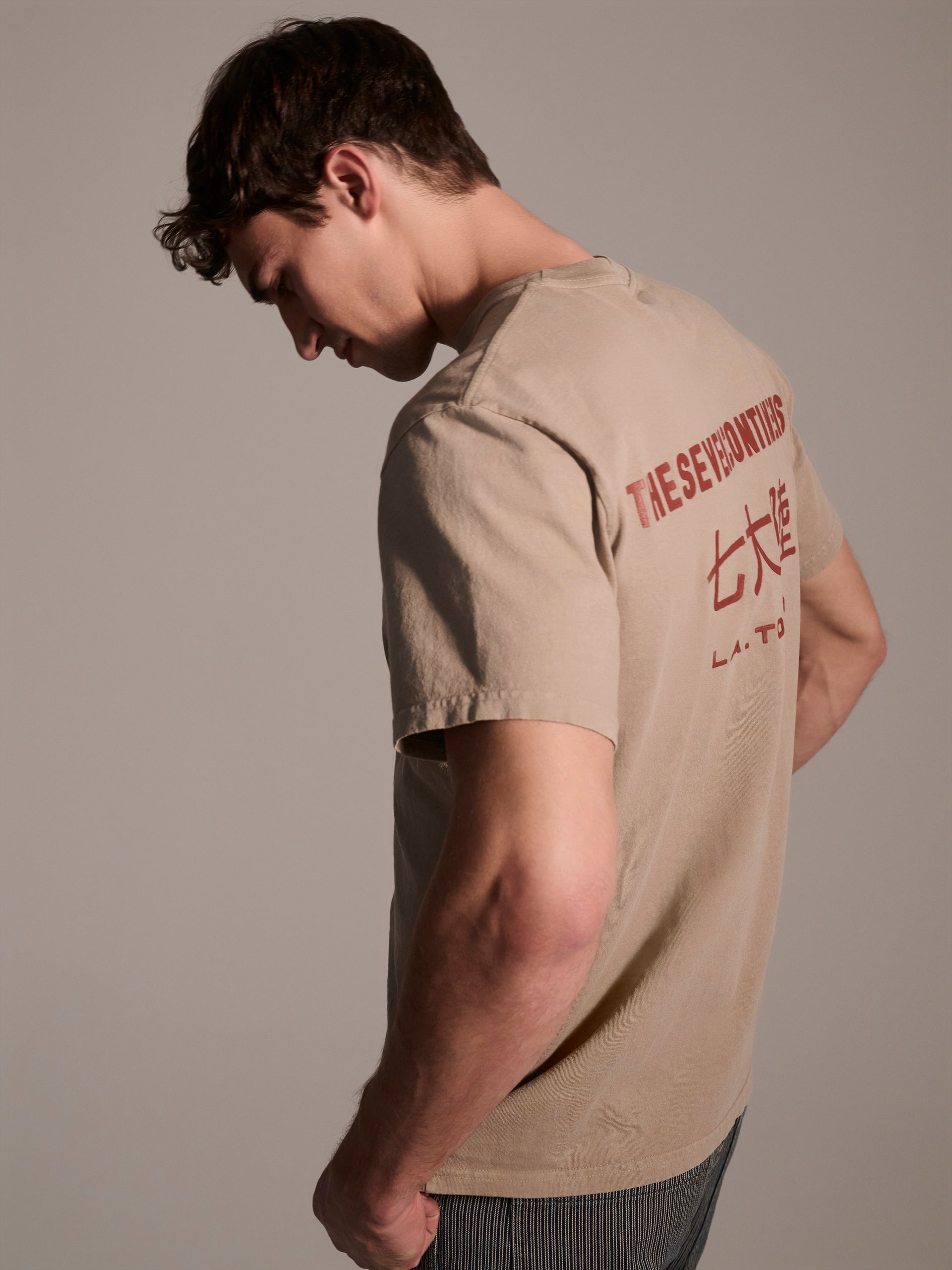 A profile image of a male model in a beige t-shirt with a red logo detail