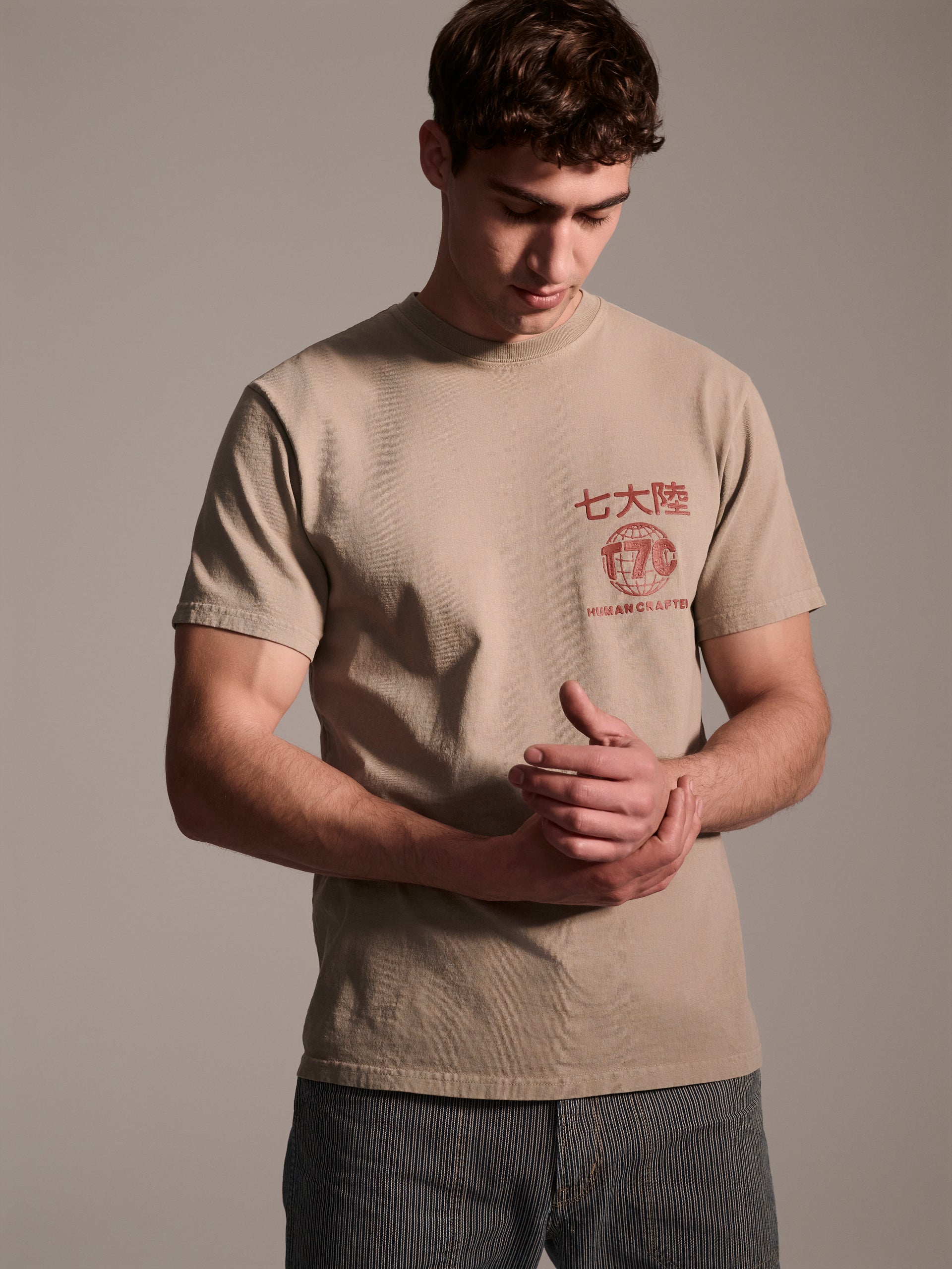 A male model in a beige t-shirt with a red logo detail