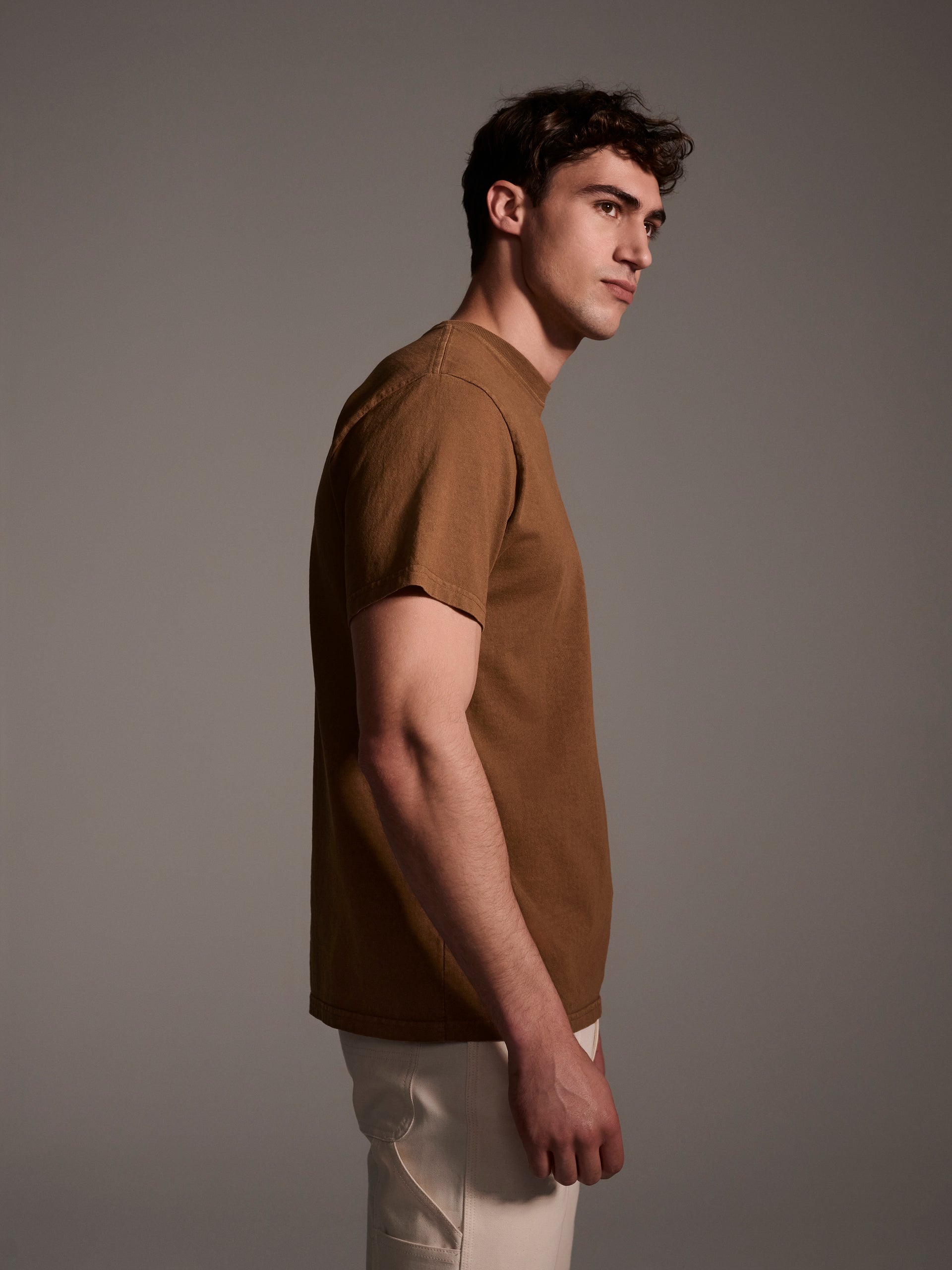 A profile image of a male model wearing a brown t-shirt with a logo detail