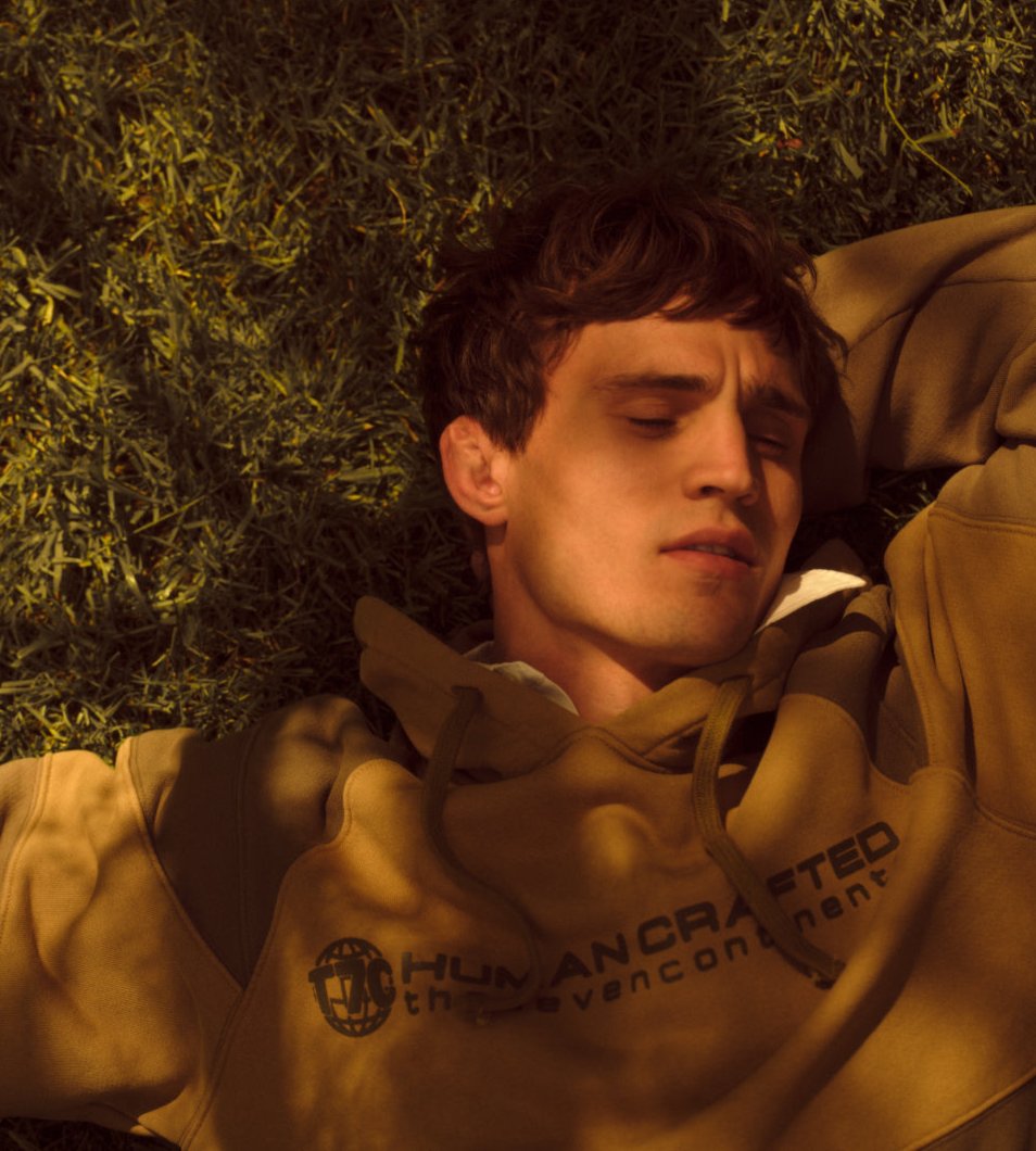 A male model wearing a hoodie napping in a garden