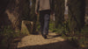 A male model wearing a railroad striped jacket and relaxed denim jeans walking in a garden