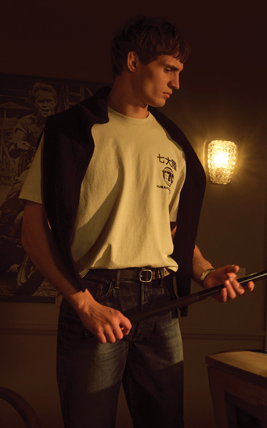 A male model wearing a t-shirt and jeans playing pool in a dark room