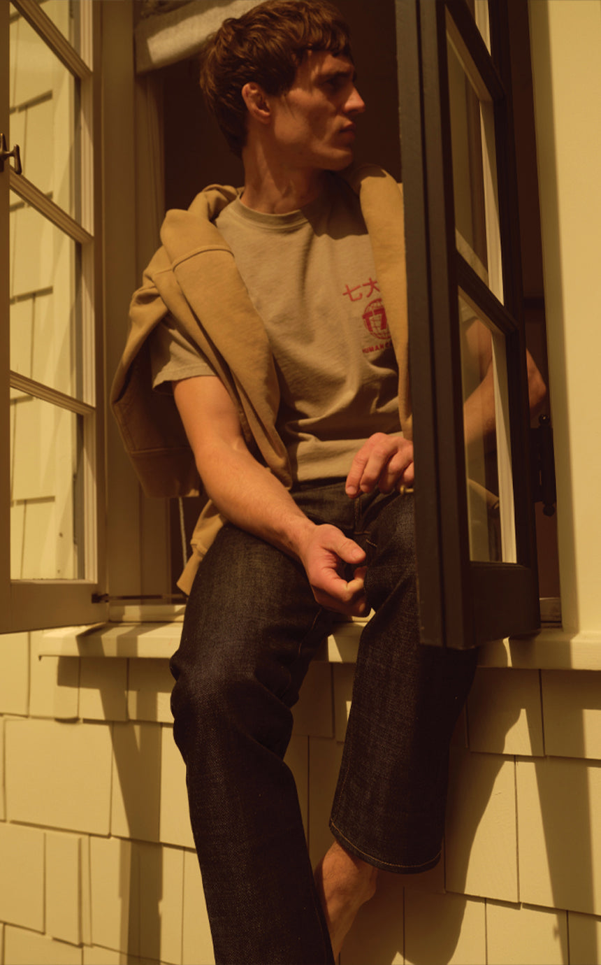 A male model wearing a t-shirt and jeans sitting on a window sill