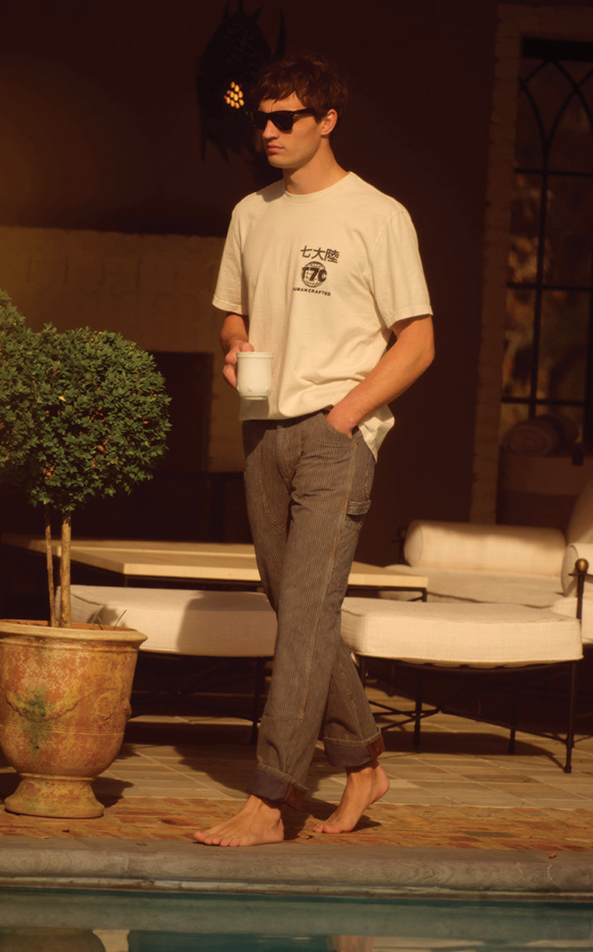 A male model wearing a t-shirt and rail road striped pants walking by a pool